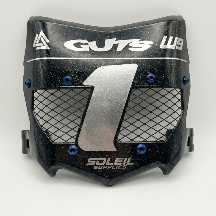 A black motocross or off-road mouthguard with a silver mesh front grille, blue hex screws, and white branding for 'GUTS' and 'Soleil Supplies'.