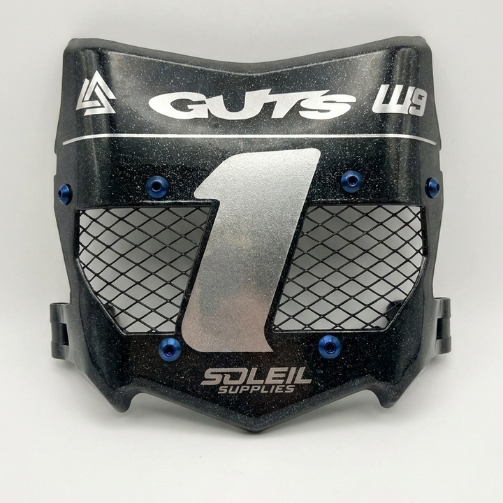 A black motocross or off-road mouthguard with a silver mesh front grille, blue hex screws, and white branding for 'GUTS' and 'Soleil Supplies'.