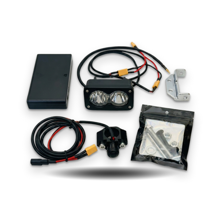 A dual LED off-road light kit with a black rectangular housing, two clear lenses, attached black wiring with yellow connectors, a black battery or power box, mounting hardware, and a bag of screws and washers, all arranged on a white background.